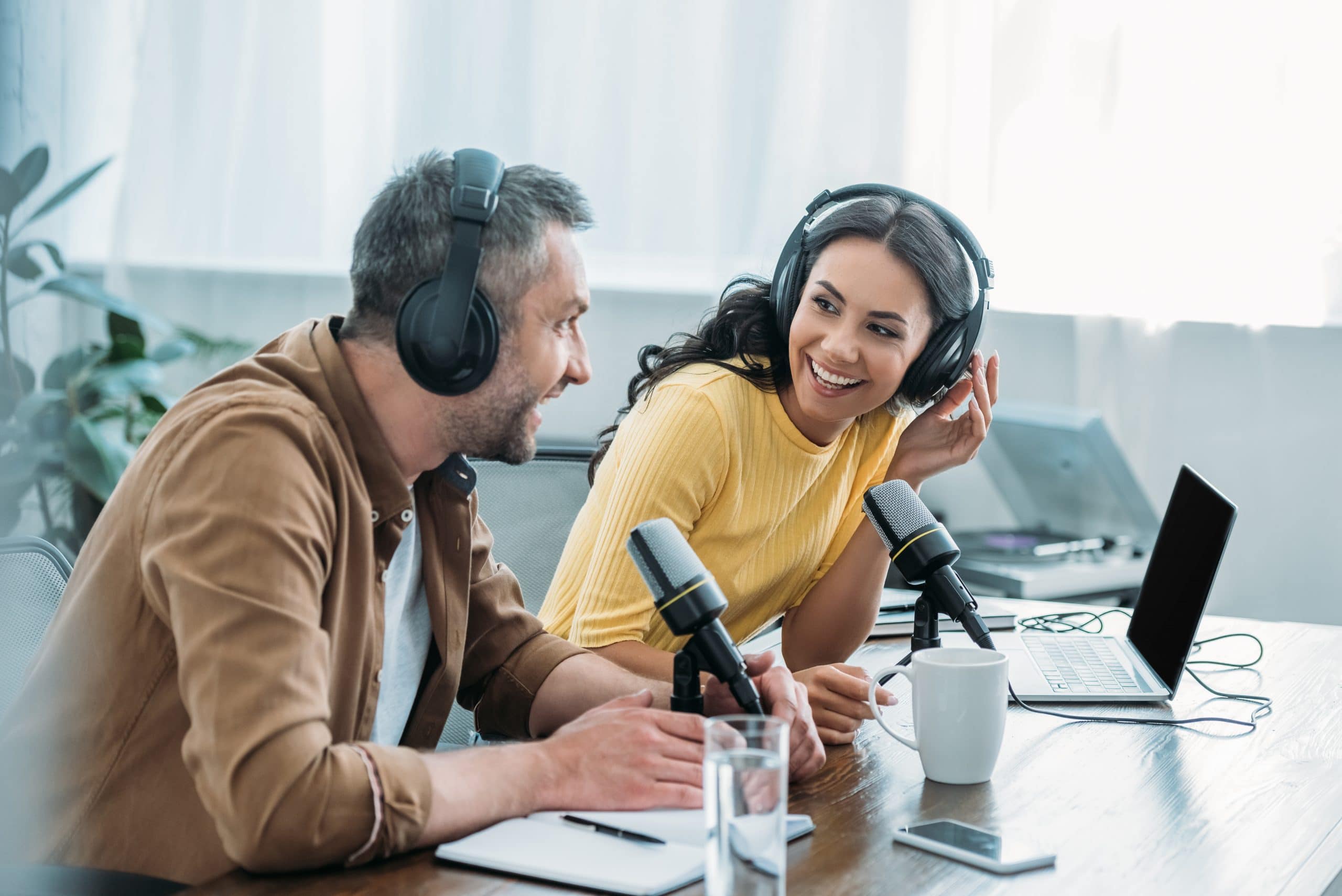 two smiling radio hosts talking while recording podcast in studio together